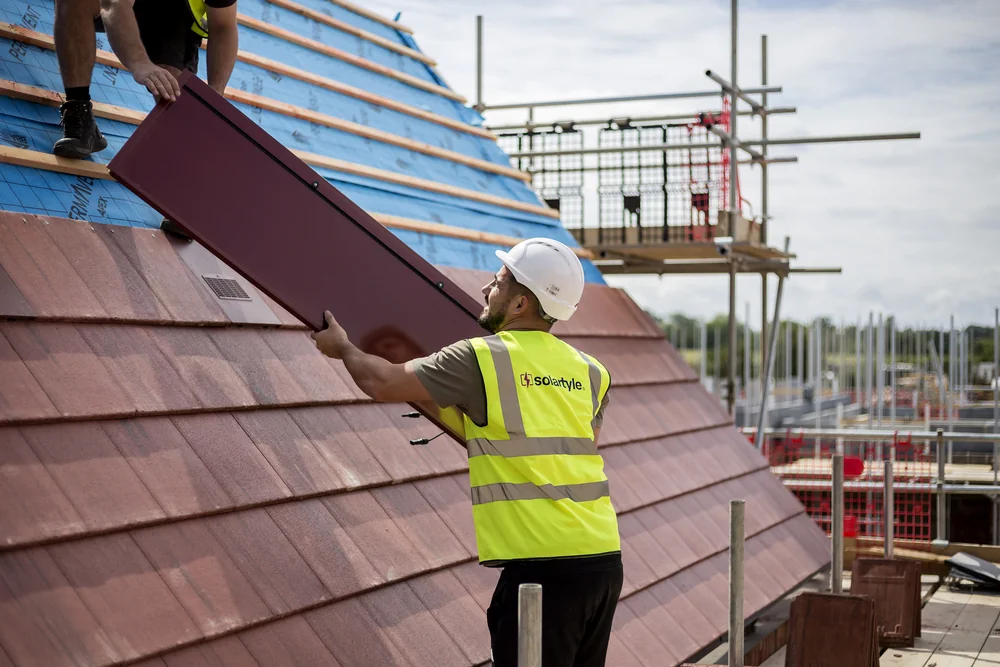 A red SolarTyle module being passed into position on the roof at Moor Hall