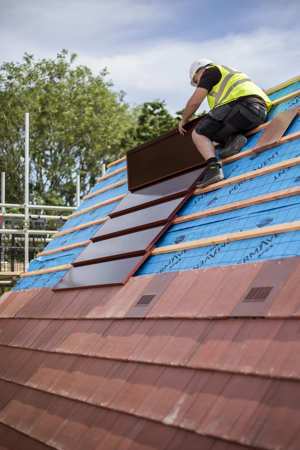 An installer positioning a red SolarTyle module during roof construction
