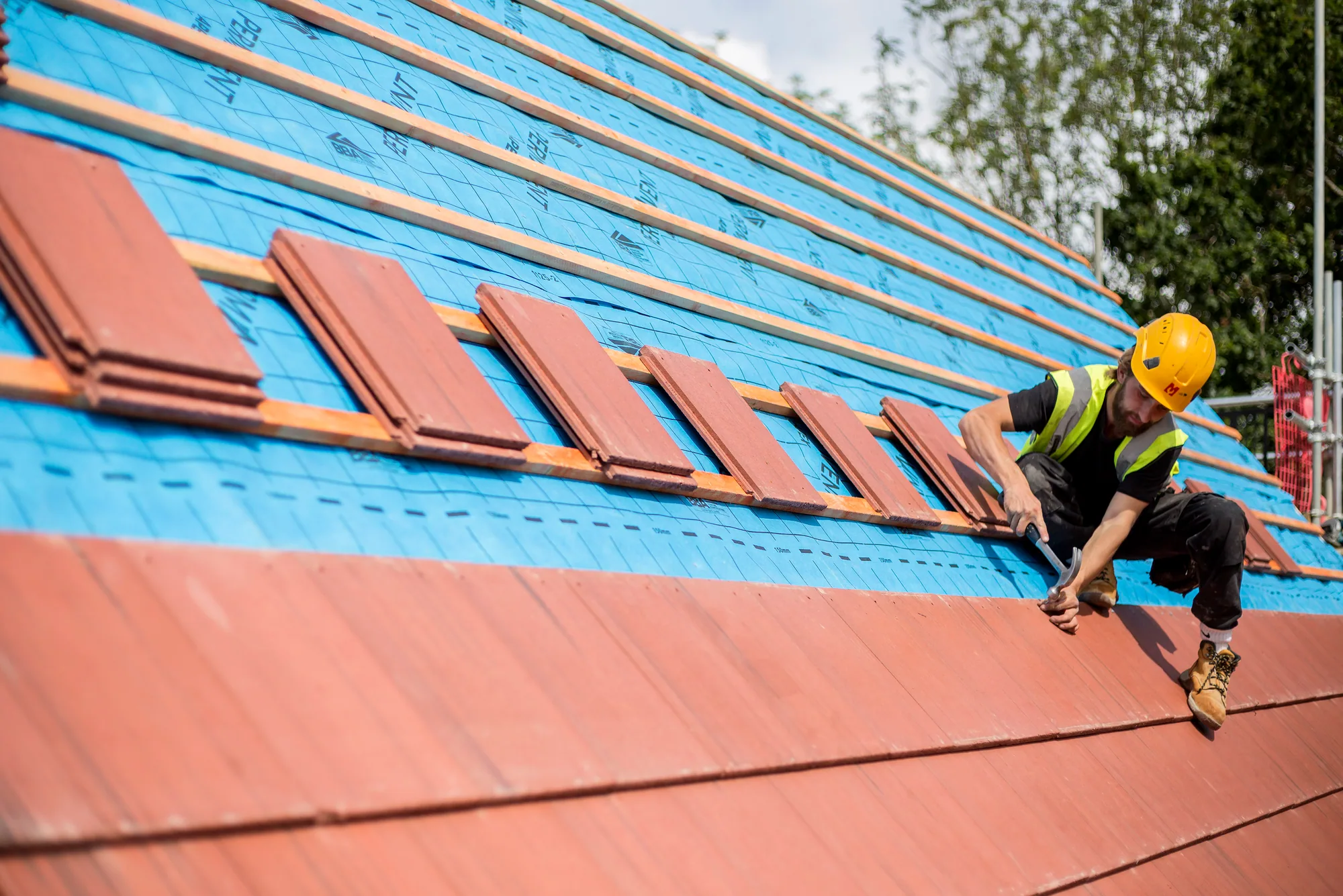 Roofer installing integrated red solar tiles across straight timber battens